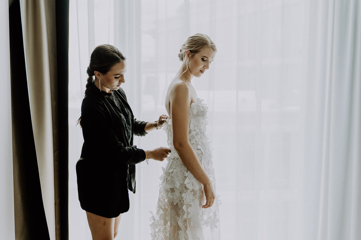 Trauzeugin hilft der Braut beim Brautkleid anziehen im Andaz Vienna Hotelzimmer beim Getting Ready für die Hochzeit by Kamerakinder Weddings
