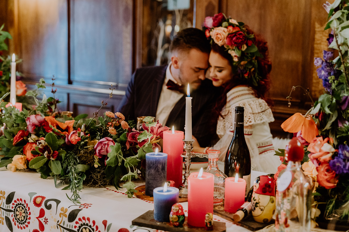 Hochzeitsinspiration Brautpaar sitzt am Brauttisch mit vielen Kerzen, viel bunter Dekoration und bohemian Flair und ganz viel Blumenschmuck boho Tischdekoration